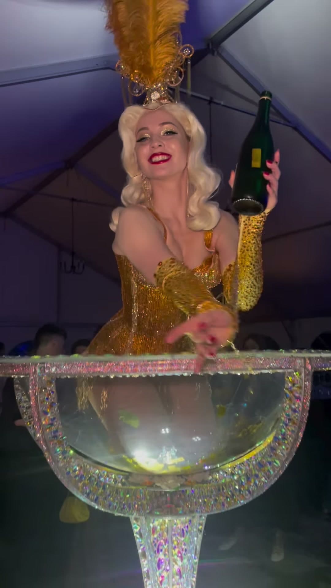 Giant champagne glass showgirl with feathered headdress pouring champagne at a luxury event in New York