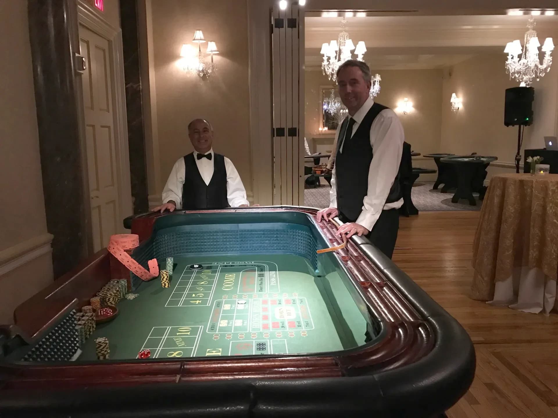 Professional casino dealers at a craps table with chips on the felt in an elegant chandelier ballroom