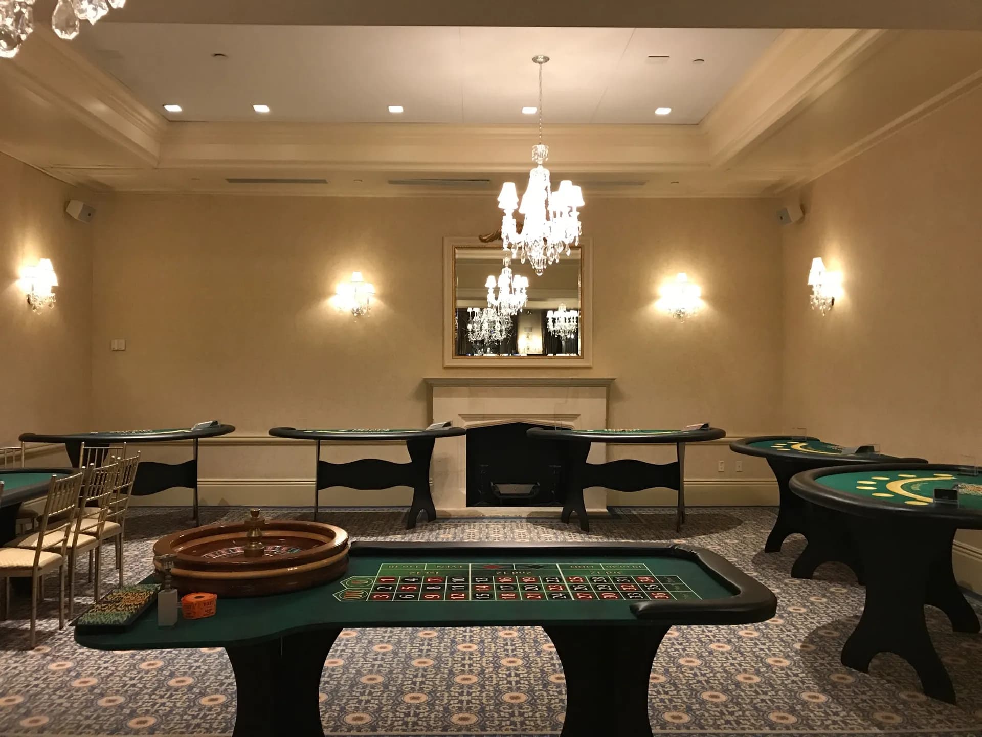 Roulette and blackjack tables set up in an elegant chandelier ballroom for a casino party