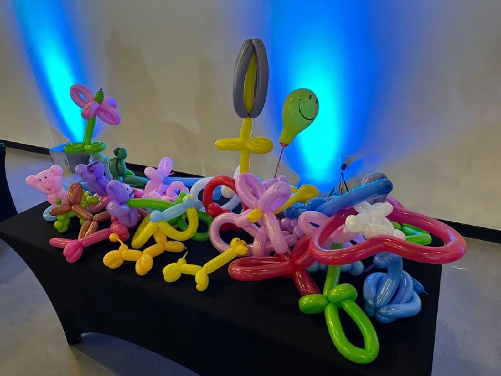 Colorful balloon animal sculptures including a bear, flowers, and a dog displayed under mood lighting at an event