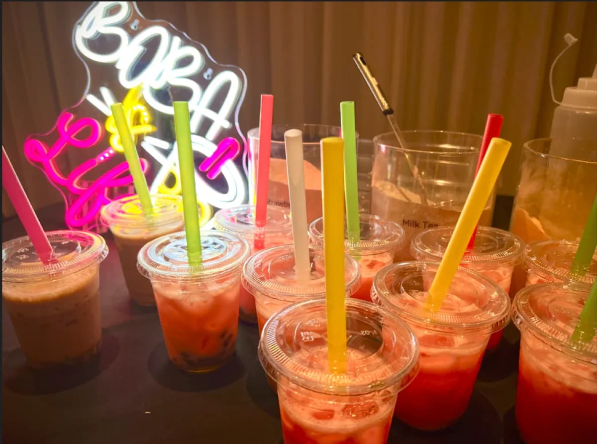 Iced boba tea drinks with colorful straws lined up under a neon Boba Life sign at a private event