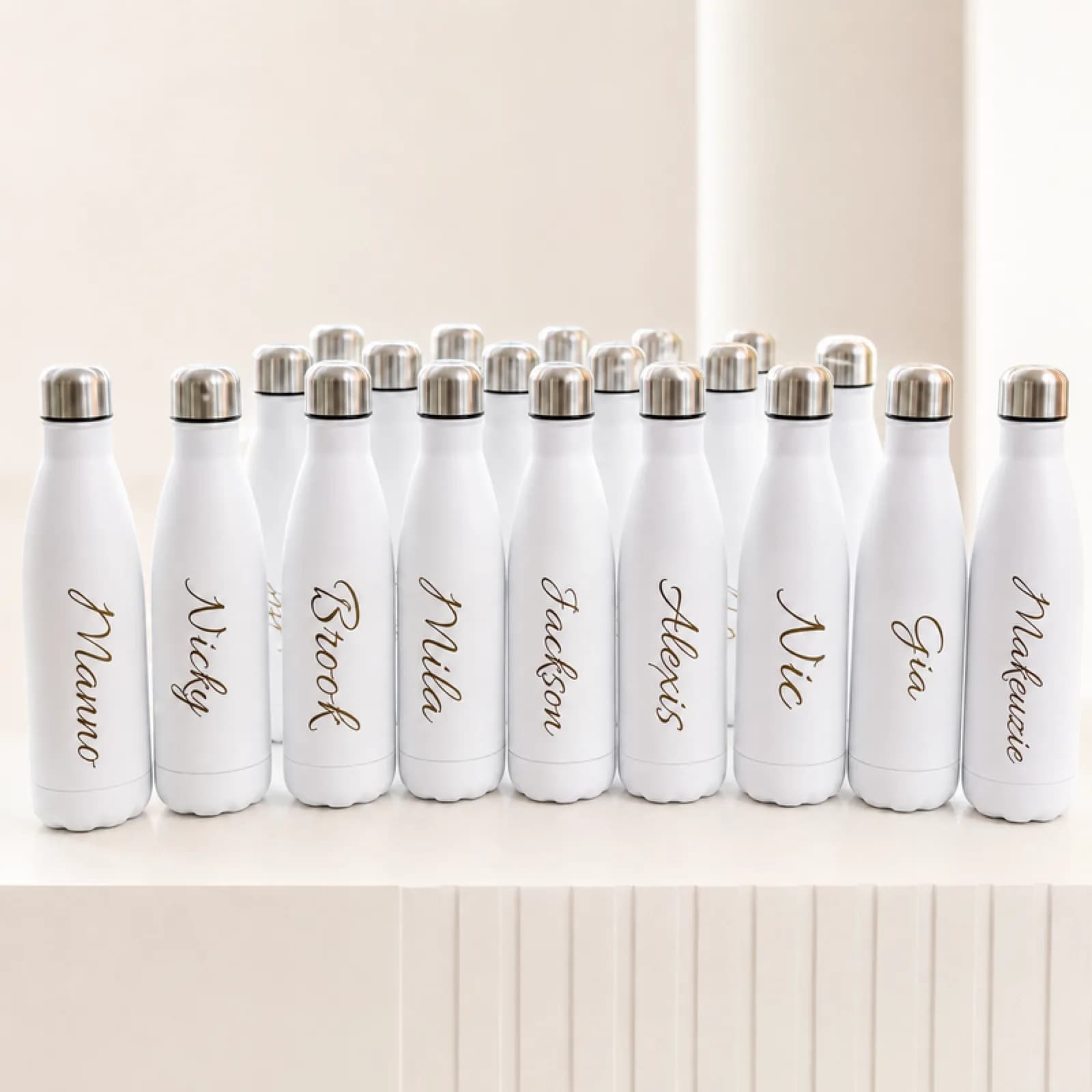 Row of white water bottles engraved with guest names displayed among white roses at an engraving station
