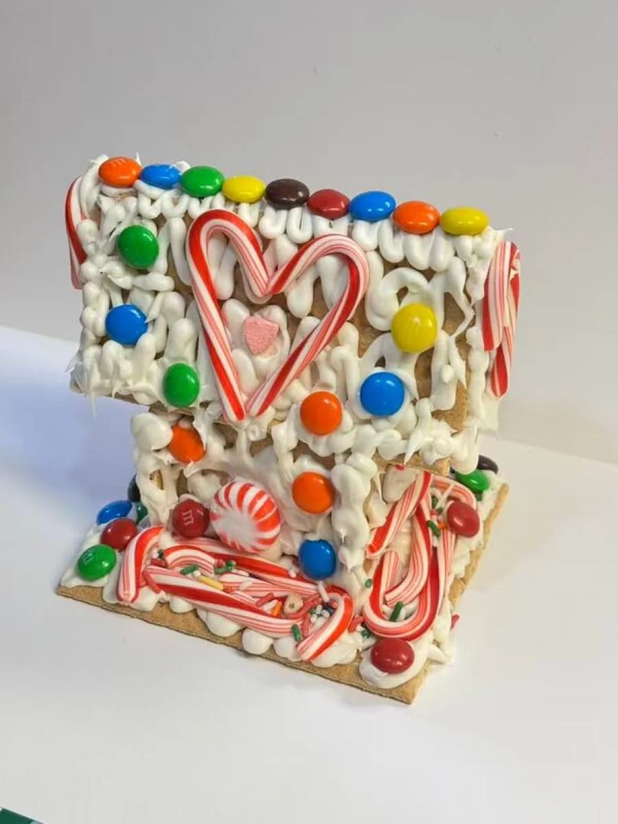 Decorated gingerbread house with white icing, a candy cane heart, and colorful candy at a holiday craft station