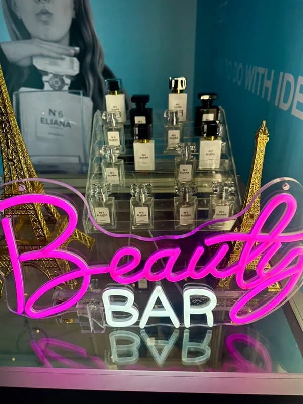 Personalized bottled fragrance display beside a glowing Beauty Bar sign and gold Eiffel Tower accents