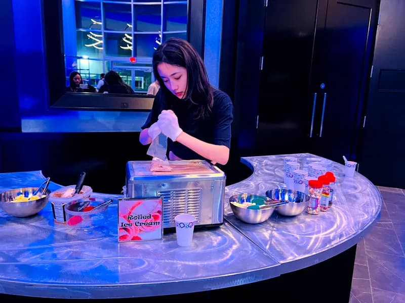 Attendant preparing rolled ice cream at a branded station during an evening event