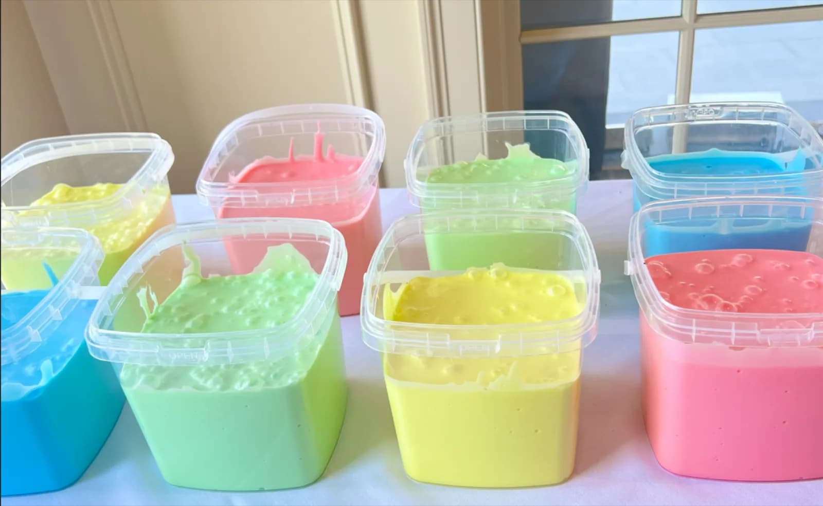 Rows of colorful mixed slime in containers ready for guests at a slime bar station