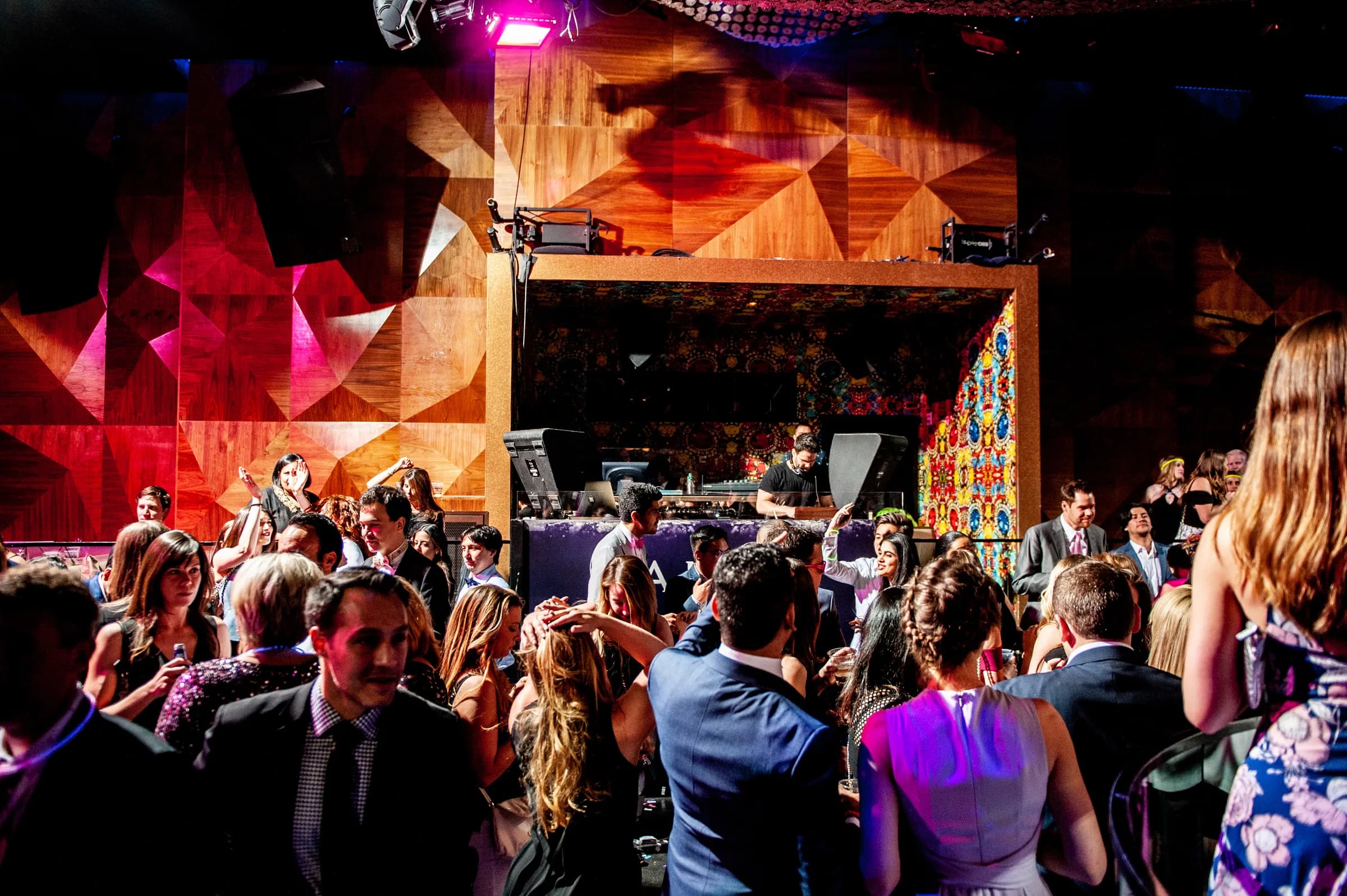A packed dance floor at a Nicholson Events DJ set, guests dancing in a warm wood paneled room with the DJ booth lit in the center