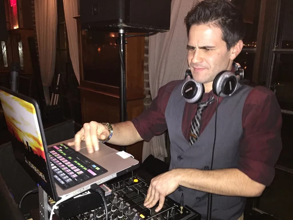 DJ Gabriel in a maroon shirt, grey vest, and tie working the decks at an intimate lounge event