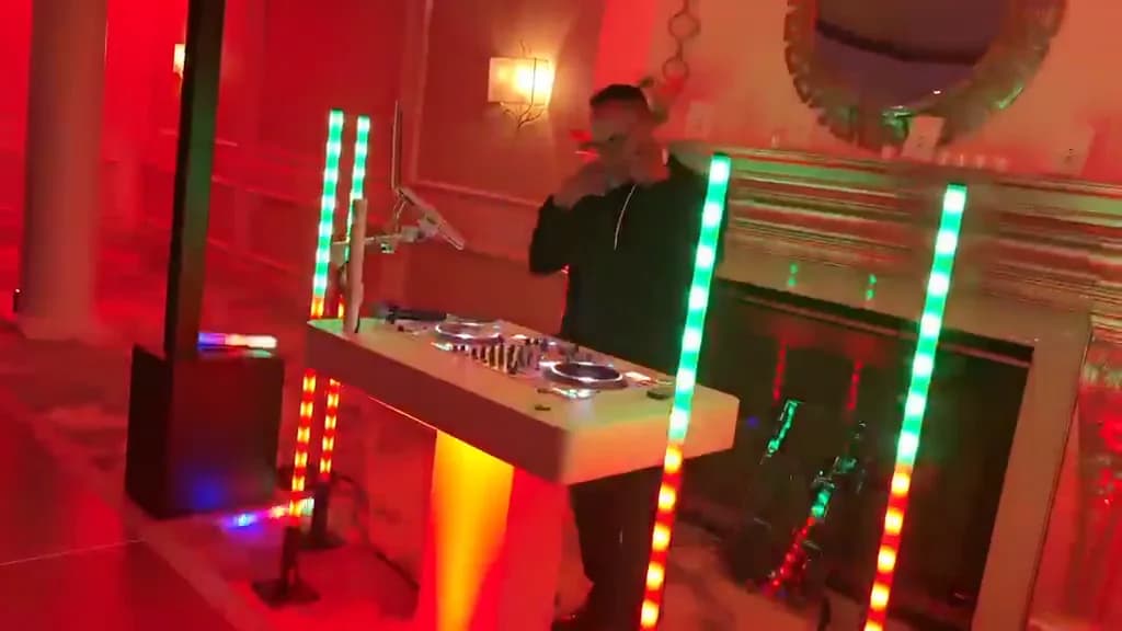 Omar behind a white LED DJ booth in a ballroom lit red and blue, guests on the dance floor