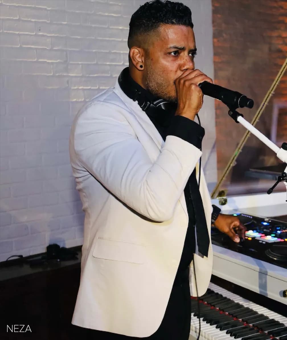 DJ Neza in a white jacket on the microphone as MC at a New York celebration
