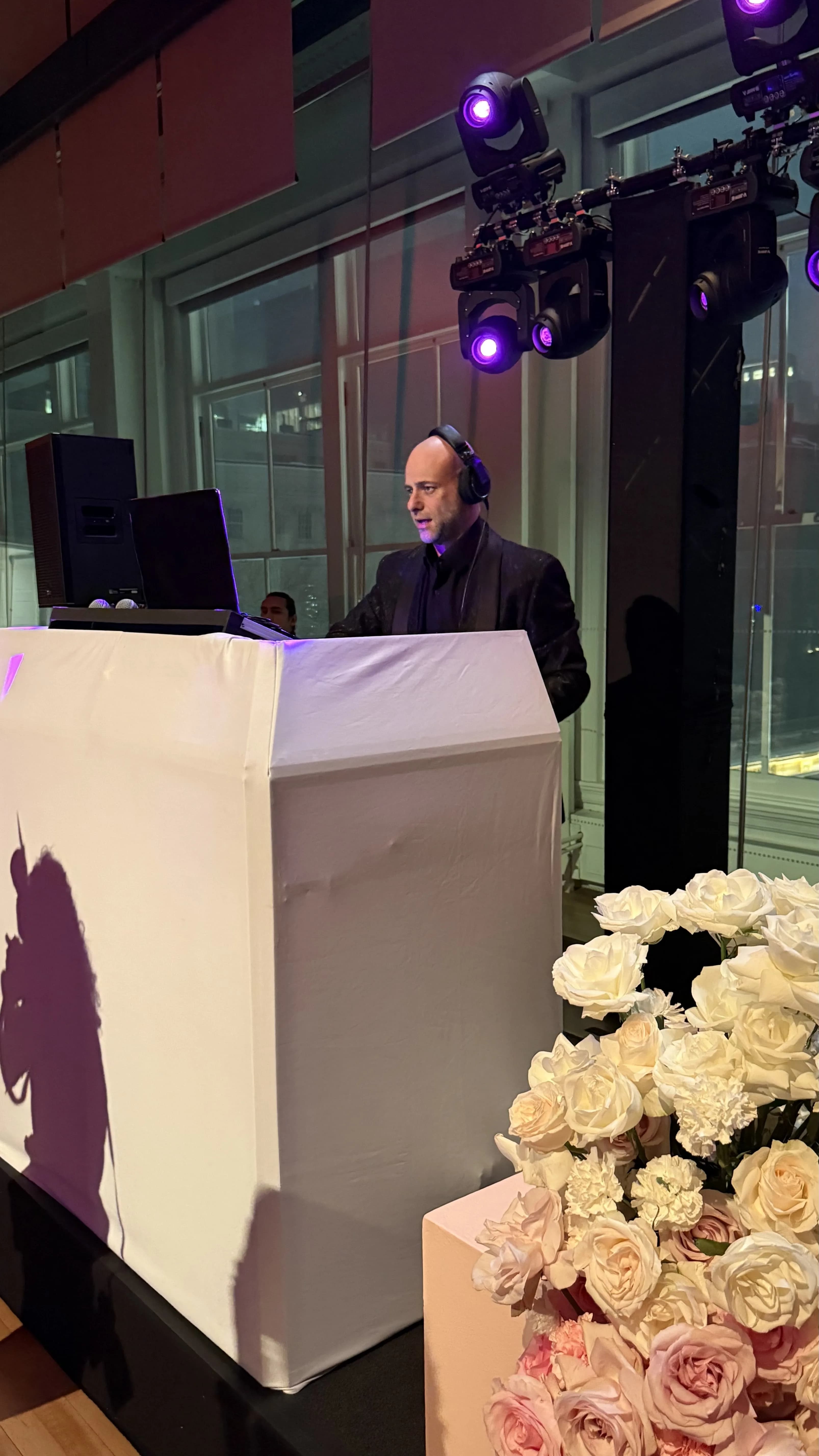 Shiran Nicholson at the DJ booth beside an arrangement of white roses at an elegant upscale venue
