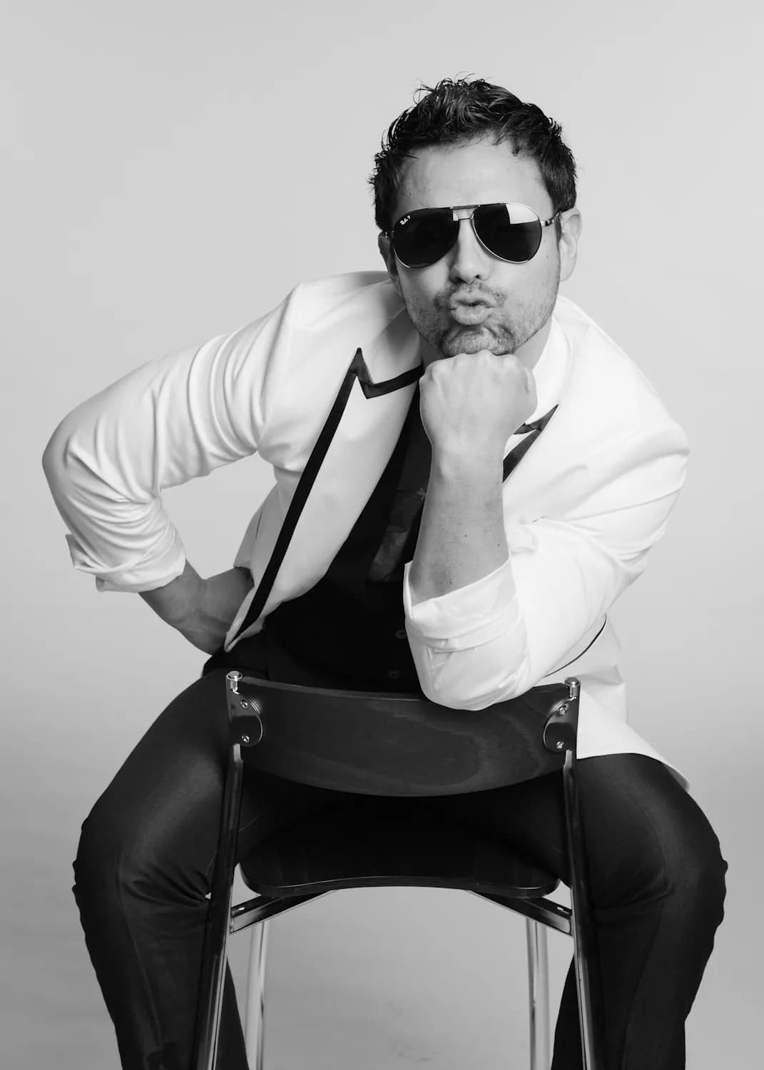 MC Nelson in a black-and-white portrait, white jacket with sunglasses, seated with confident pose