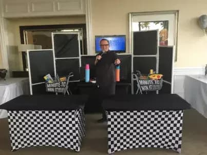 Minute to win it game station at an event with a host and two checkered competition tables, fast-paced 60-second party challenges