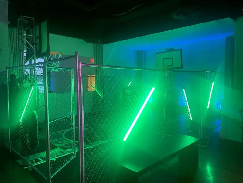 Rage in a cage enclosed basketball court at an event, a chain-link cage lit with neon green and blue LED tubes for street-style 3-on-3 play