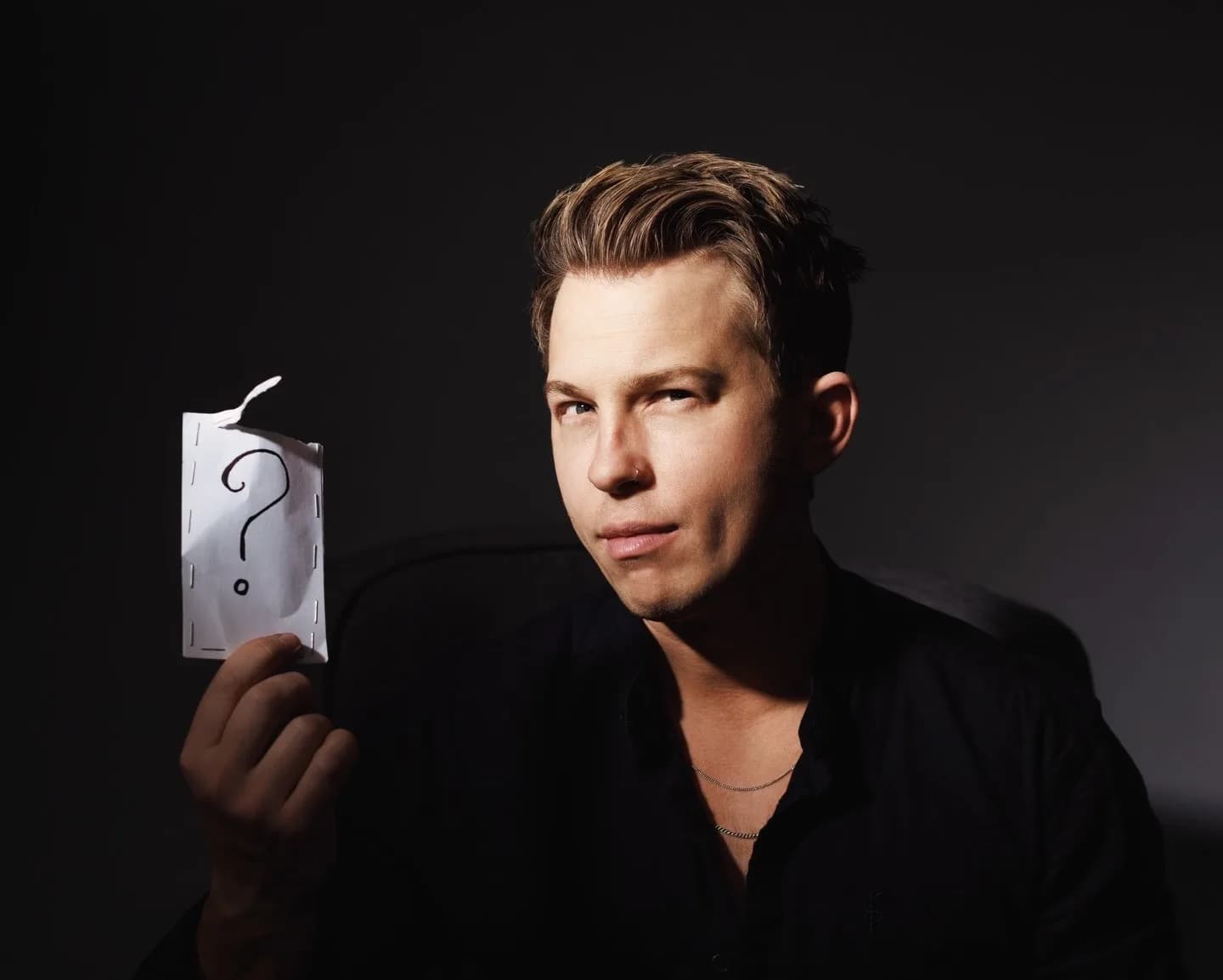 Kevin, the Modern Mentalist, holding a question mark card beside his face in a dramatic dark portrait