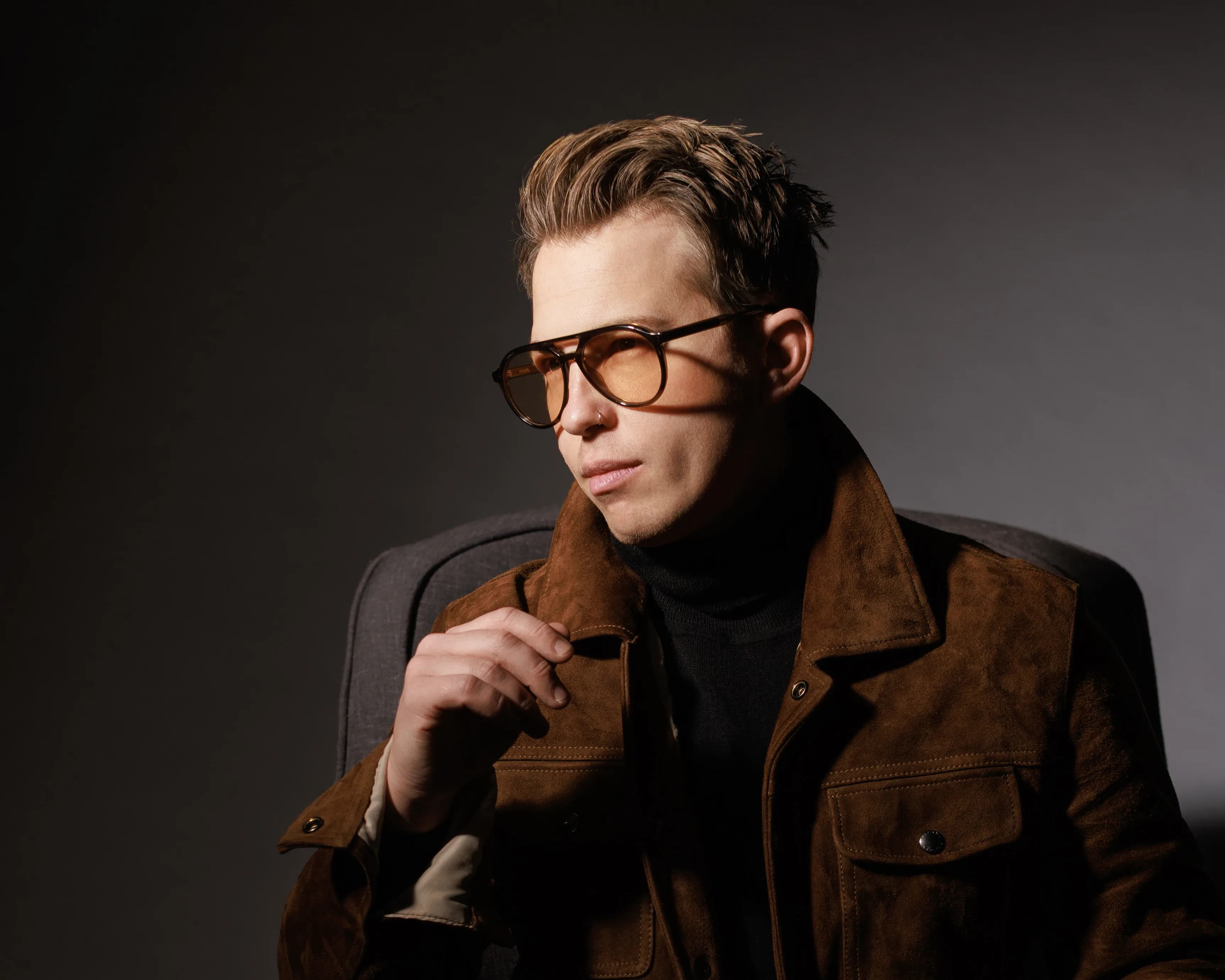 Editorial portrait of Kevin, the Modern Mentalist, in a suede jacket and tinted glasses against a moody backdrop