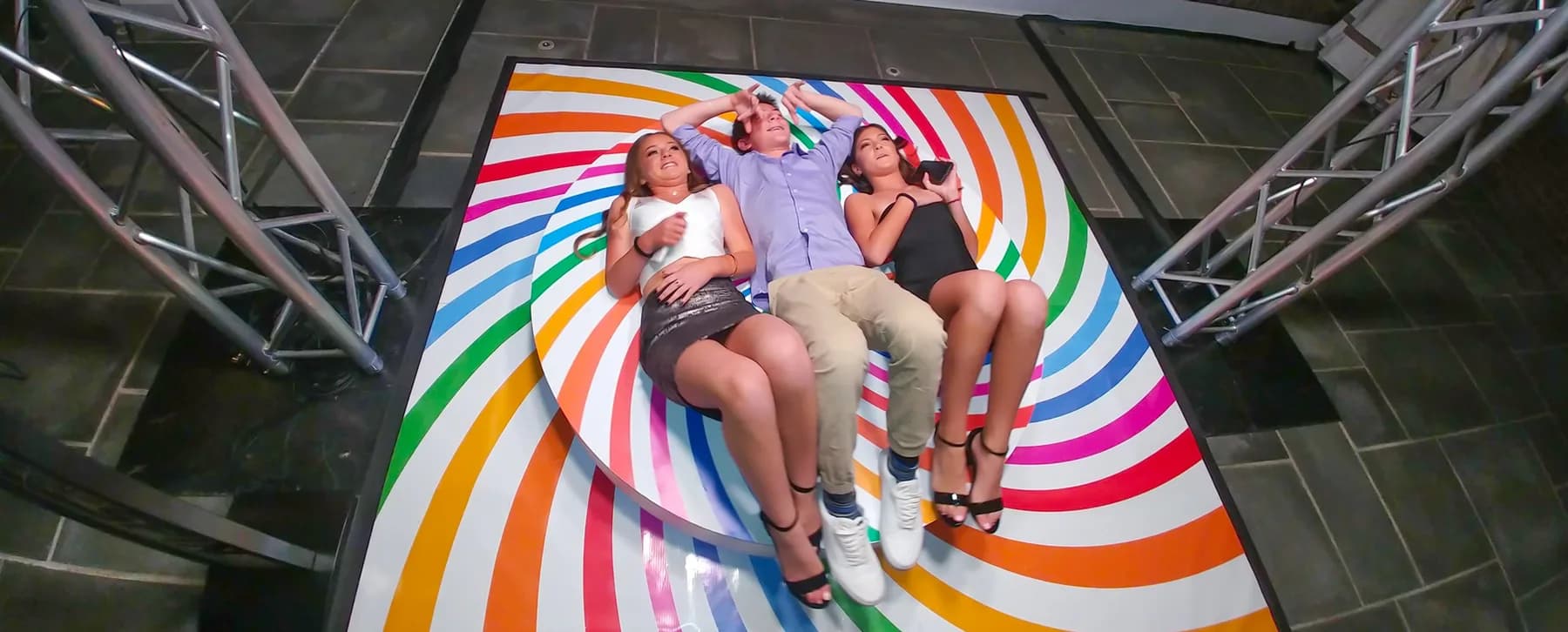 Overhead camera view of three guests laughing on the colorful top-spin platform during a sweet 16 event