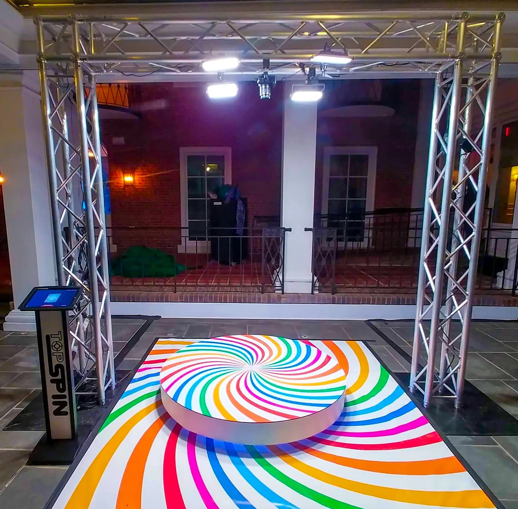Top-spin 360 photo booth rig with overhead truss camera above a colorful swirl spinning platform