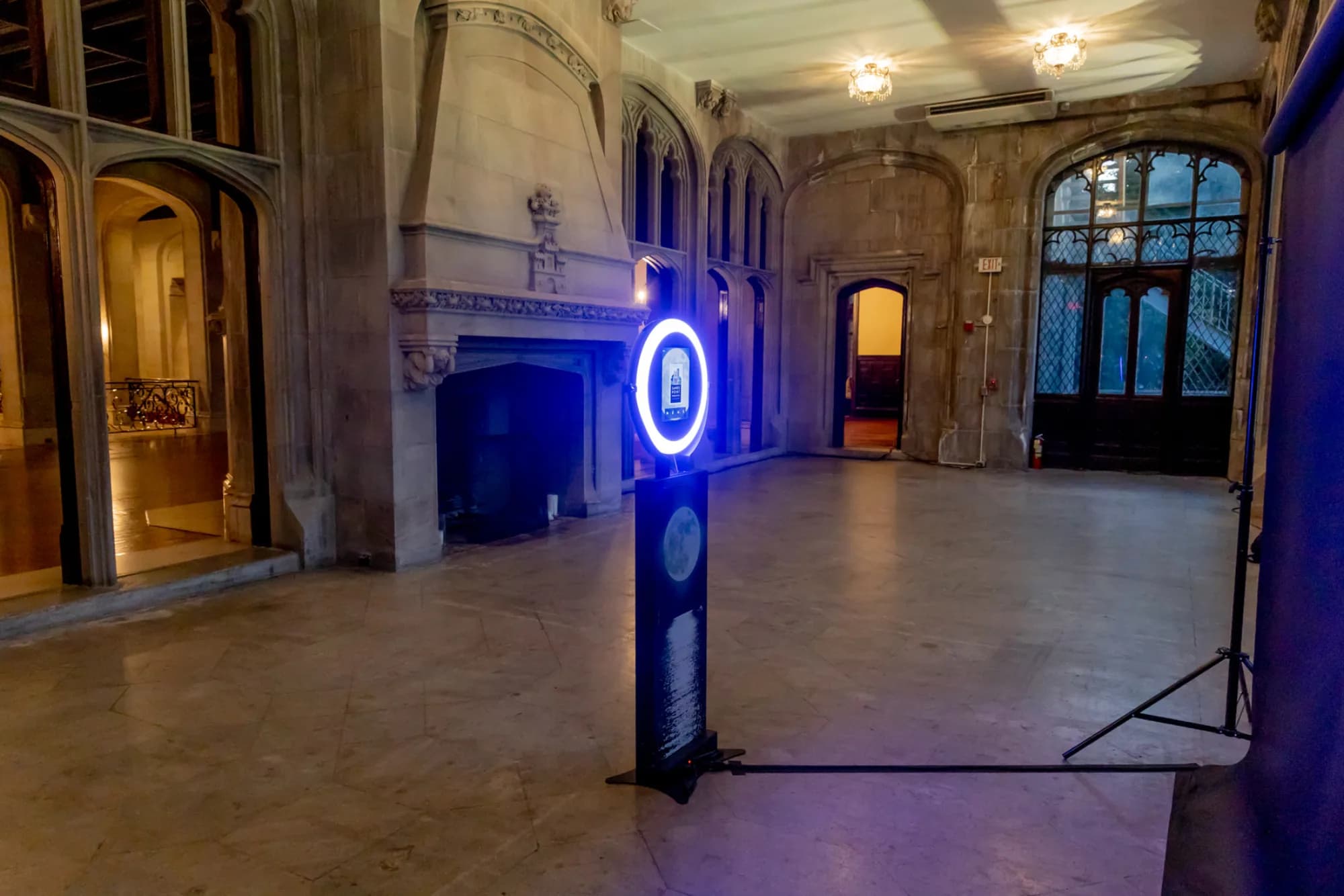BigView circular-display photo booth standing alone in a grand stone-vaulted hall lit by ambient blue ring light