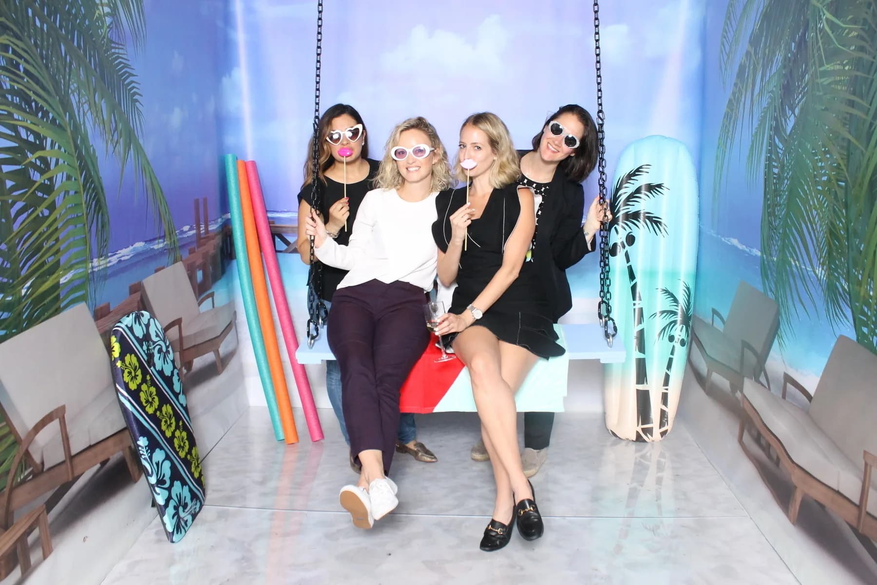 Three guests posing on a suspended photo swing inside a tropical beach-themed immersive room at an event