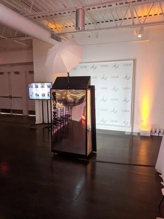 Mirror photo booth setup with step-and-repeat backdrop and photo gallery display monitor at an event