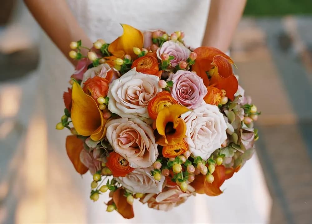 Bridal bouquet of blush roses and orange calla lilies held against the bride’s white gown