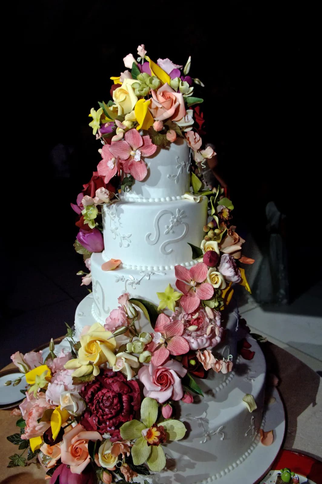 Four-tier white wedding cake with monogram piping and cascading fresh flowers