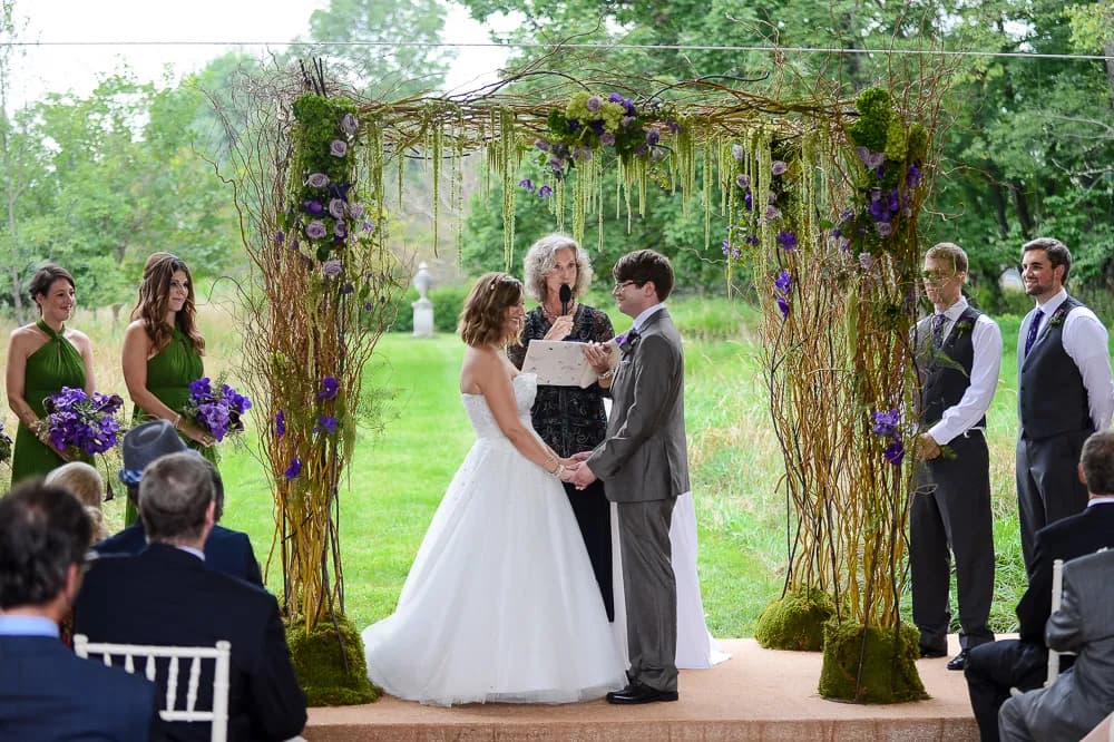 Outdoor wedding ceremony under a birch arch dressed with green and purple flowers