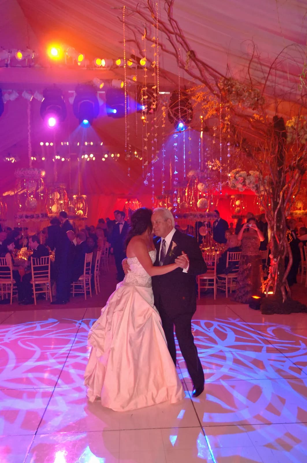 Bride dancing with her father under pink and purple gobo lighting with hanging crystal decor