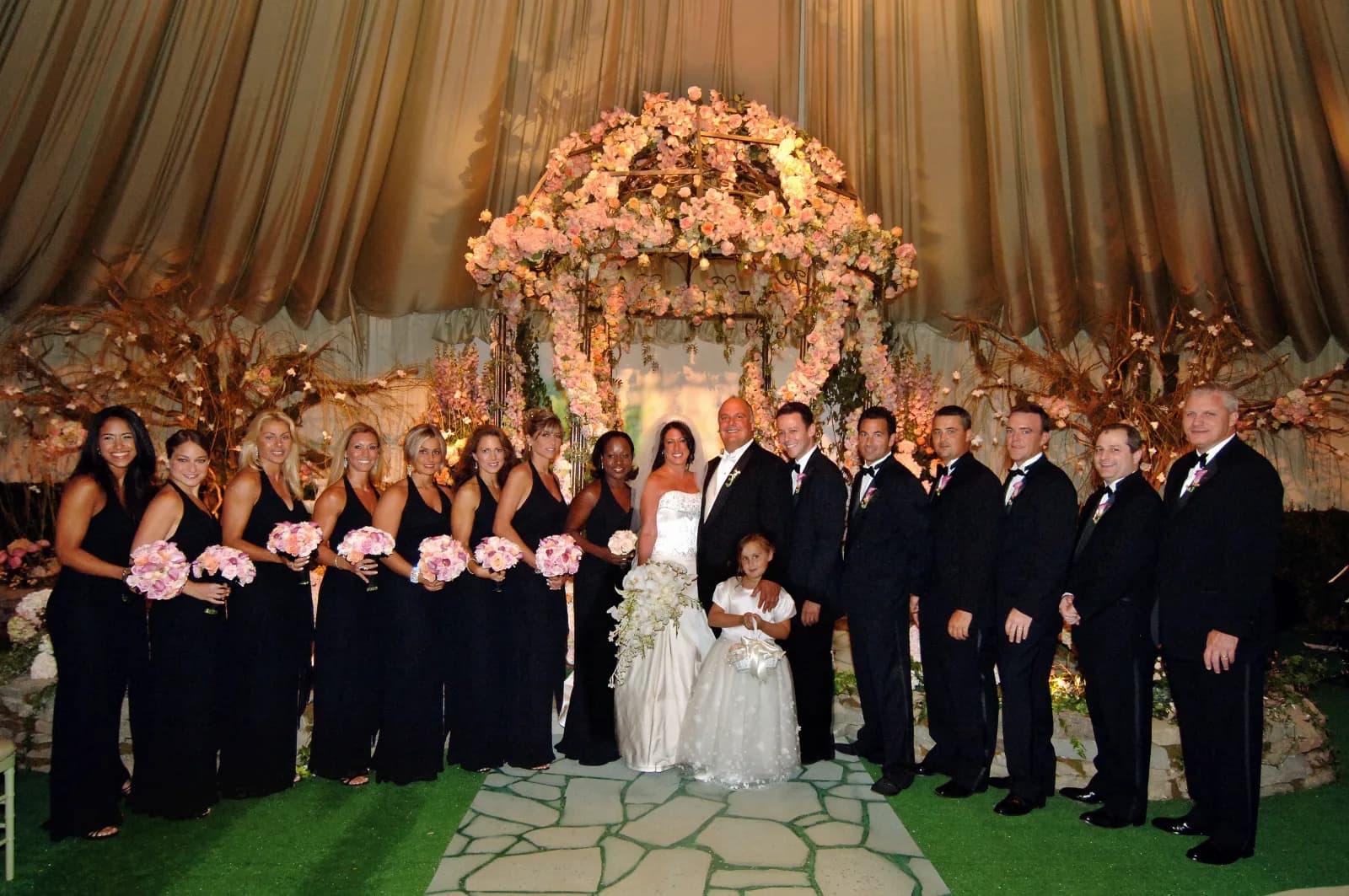 Full wedding party under a floral-covered chuppah inside a gold-draped tent