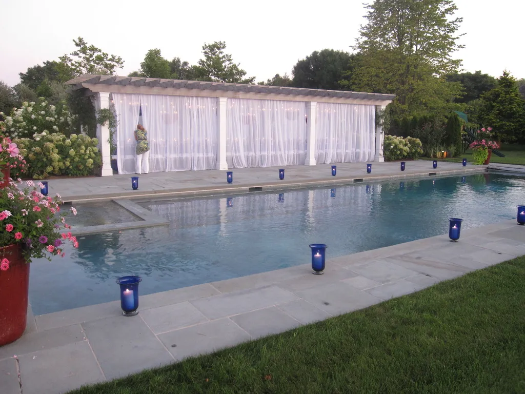 Pool framed by a white draped pergola and blue votive candles at dusk at a Hamptons summer party