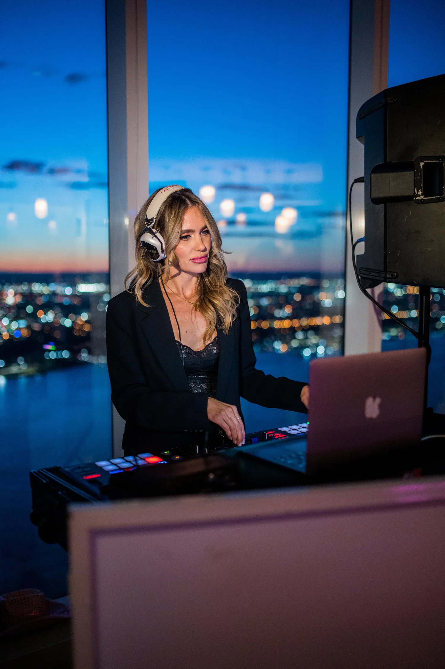 DJ Dani at the decks in front of a floor-to-ceiling nighttime NYC skyline at an upscale private event